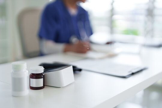 Blurred healthcare professional writing patient notes on desk with medication bottles medical office clinic setting