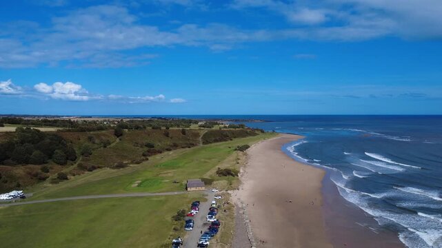 Aerial panoramic view of Alnmouth beach in bright summer sunlight with waves on the blue sea and surrounding coastal landscape