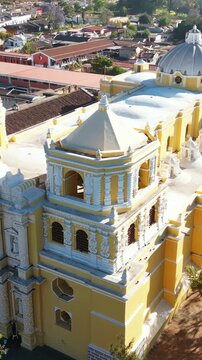 Aerial drone view of the iconic yellow La Merced Church in Antigua Guatemala surrounded by colonial buildings and palm trees. Vertical