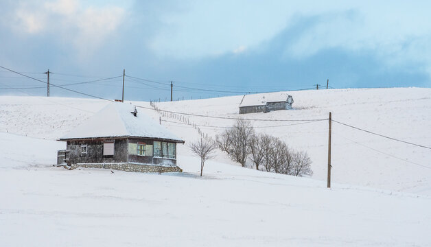 Remote rural farmhouse and barn in snowy winter landscape with power lines under cloudy blue sky