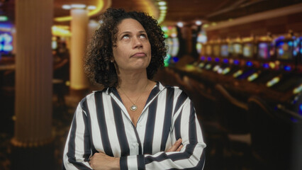 Obraz premium Woman wearing striped shirt crossing arms in front of illuminated slot machine row at casino; rejection.