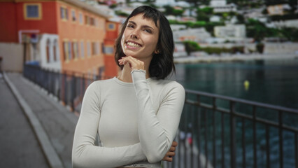 Obraz premium Young hispanic woman with hand on chin gesture on a colorful street lined with buildings; quiet reflection.