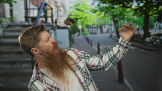 Young bearded man miming guitar playing with right hand strumming gesture on street; joyful creativity imagination.