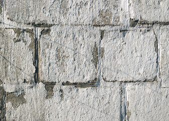 A cracked, light gray, almost white cinder block wall coated with acrylic-based chalk-lime paint. The texture of the old stone surface. Close-up.