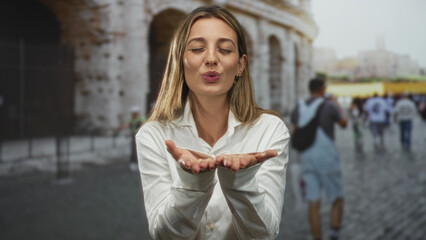 Plakat Woman blowing a kiss with cupped hands in front of the colosseum building in rome among tourists; playful romance.
