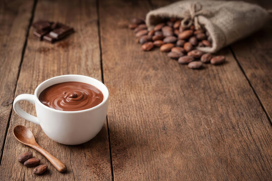 Tazza di cioccolata calda densa su tavola di legno rustica con fave di cacao e sacchetto di juta. Generative AI 