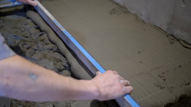 Close-up of master using aluminum straightedge to create even mortar layer for shower tray mounting.