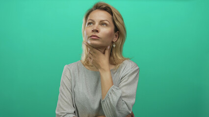 Fototapeta premium Woman touches chin in green studio while tilting head upward with thinking gesture and steady gaze; curiosity.