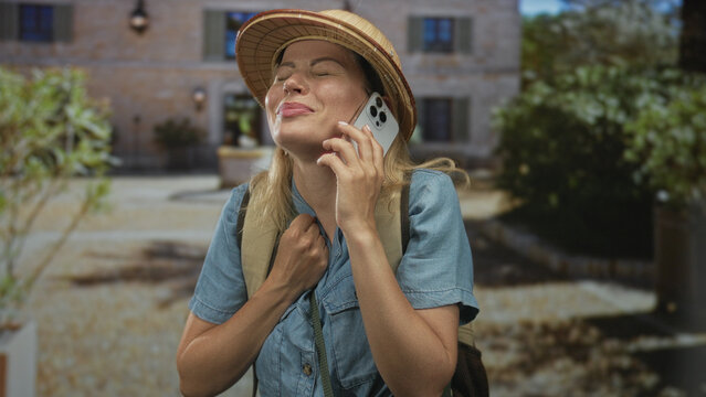 Woman wearing pith helmet holding smartphone to ear at sunlit building entrance outdoors; adventure exploration wanderlust relief.