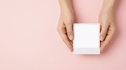 Obraz premium Blank polaroid photo frame held in hands on soft pink background mockup for memory, photography or branding design perfect for Mother’s Day concept