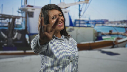 Fototapeta premium Middle age brunette woman smiling and making hand gesture to camera in studio with boat backdrop; friendly.
