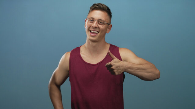 Man giving two thumbs up and smiling in studio blue backdrop with maroon tanktop and glasses; happiness positivity encouragement approval.