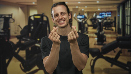 Fototapeta premium Man smiling and showing finger heart with hands in a studio gym setting, long hair visible and forearms bare; joy connection.
