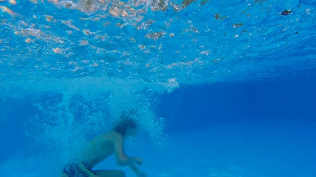 Father and his ten year old son having fun in a swimming pool, dad tossing the boy into water as he dives. Joyful family leisure and active summer recreation. Slowmotion video.
