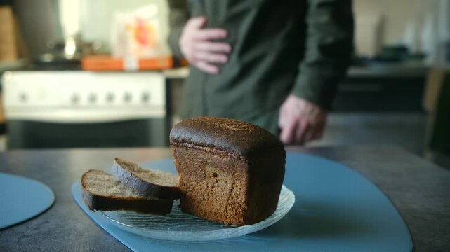 Unfocused man clutching his stomach in pain from hunger or digestive problems, with fresh loaf of rye bread on kitchen table in foreground, showing concept of indigestion. Gluten intolerance concept