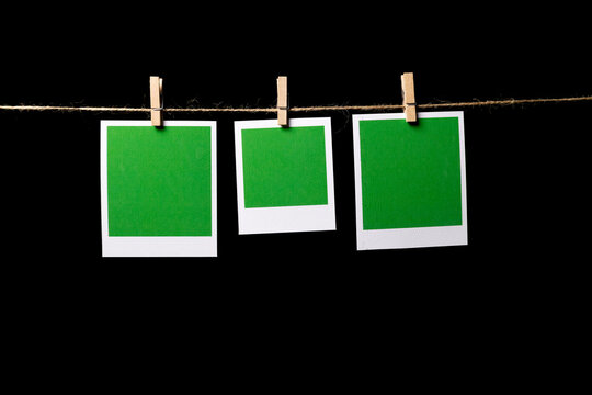 Three green rectangular sheets of paper in a white frame hang from a thin thread against a black background, attached with a clothespin, side view. Space for text