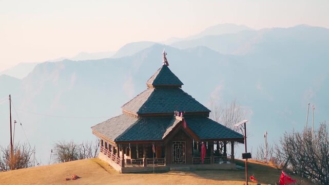Landscape shot of Hidimba Devi Temple in front of foggy Himalayan mountain range during the sunset as seen from Thachi Valley in Kullu district, Himachal Pradesh, India. Beautiful temple on mountain. 