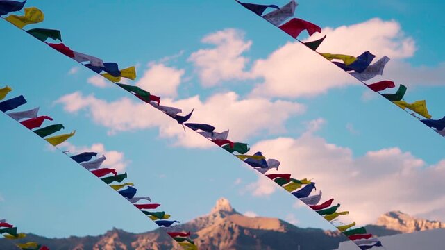Rack focus shot of Buddhist Prayer flags waving in the wind against the orange sky and dried Himalayan mountain peak during the summer season as seen from Padum in Zanskar Valley, Ladakh, India.