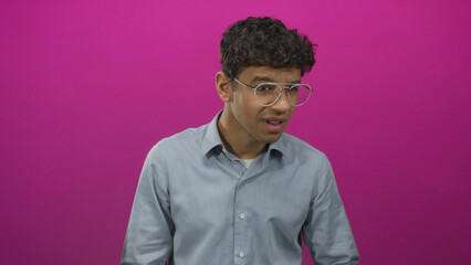 Obraz premium Young hispanic man with scrunched face holding chin with hand against vibrant pink background in studio; thought.