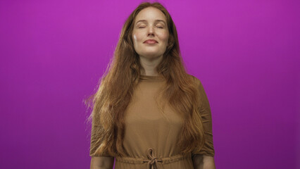 Fototapeta premium Woman with eyes closed and long hair wearing brown dress poses with gentle smile in magenta studio; serenity.