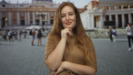 Fototapeta premium Young caucasian woman standing with hand on chin in front of a historic building entrance on cobblestone plaza; serenity.