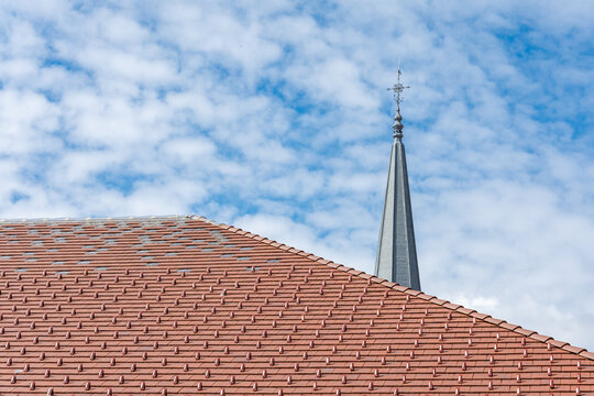 Toit en tuiles rouges avec fl&egrave;che d&rsquo;&eacute;glise sous un ciel nuageux