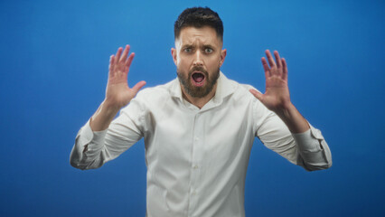 Fototapeta premium Man with beard and white shirt, hands raised and open mouth showing teeth, gesturing palms toward camera in studio; frustration.