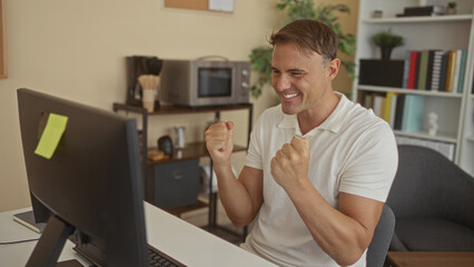 Fototapeta premium Man clenches fists and smiles at computer screen with sticky note on monitor in building office, leaning forward at desk; excitement triumph.
