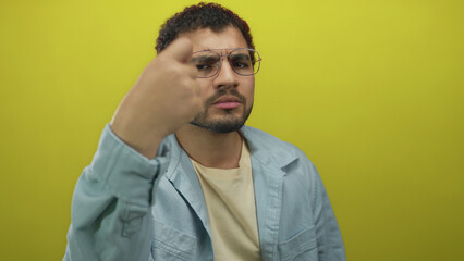 Obraz premium Man beckons hand in yellow studio with serious gaze and visible gesture near face wearing casual shirt; curiosity.