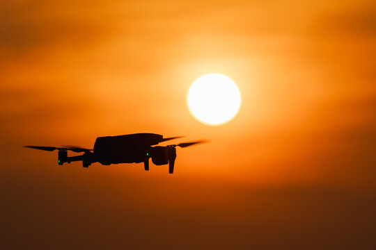 Drone silhouette flying in front of bright sun at sunset