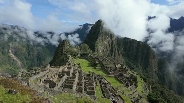Ancient Machu Picchu in Peru as clouds and mist rise through the surrounding mountains, gently enveloping the iconic Inca citadel in a dramatic and atmospheric landscape