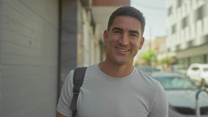 Fototapeta premium Man smiling showing face on a city street, wearing t shirt and backpack strap; confidence approachability.
