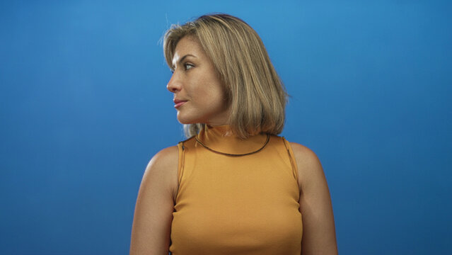 Woman with blonde bob turning head in blue studio setting, showing profile silhouette; quiet introspection.