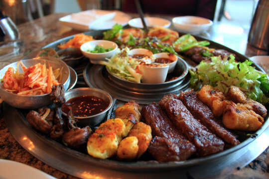 A traditional Korean cuisine feast captured in food photography: grilled meat, bibimbap, kimbap, tteokbokki, and a variety of banchan like kimchi and jorim. Rich and colorful.