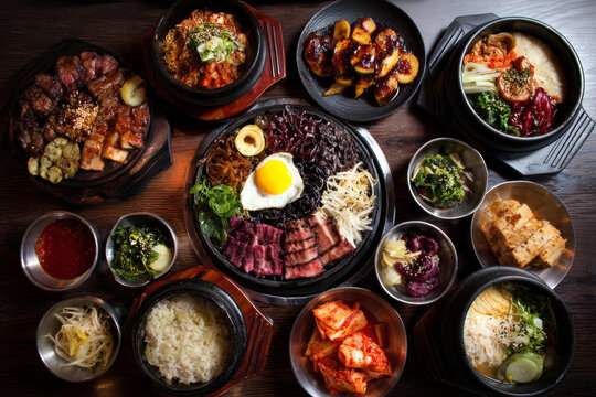 A colorful food photography spread of Korean national dishes including grilled meat, bibimbap, kimbap, tteokbokki, various sauces, and banchan like kimchi and jorim.