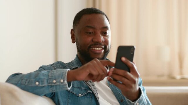 Online entertainment. Close up portrait of young carefree african american guy web surfing on smarthone at home, scrolling news in social media, tracking shot, slow motion