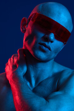 Stylish man with red sunglasses posing confidently against a vibrant blue background, showcasing a blend of modern fashion and artistic lighting.