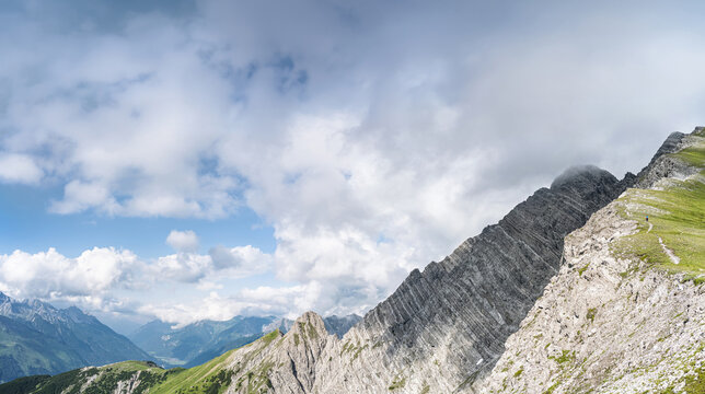 Hiker on a scenic mountain path overlooking the exposed northeast ridge of Ruitelspitze. Dramatic view of Gartenspitze peak and steep limestone faces in the Lechtal Alps, Tyrol, Austria.