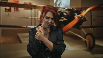Woman holding wrist in pain while clutching rings beside a vintage biplane exhibit inside museum building  injury distress. © Krakenimages.com