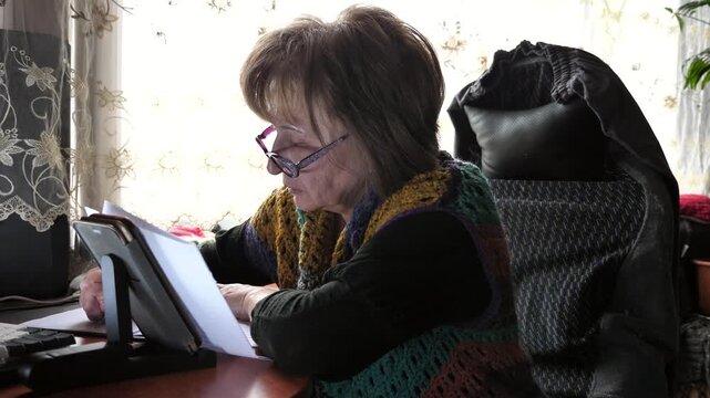 A woman writes with a pen in a notebook while sitting at a table.