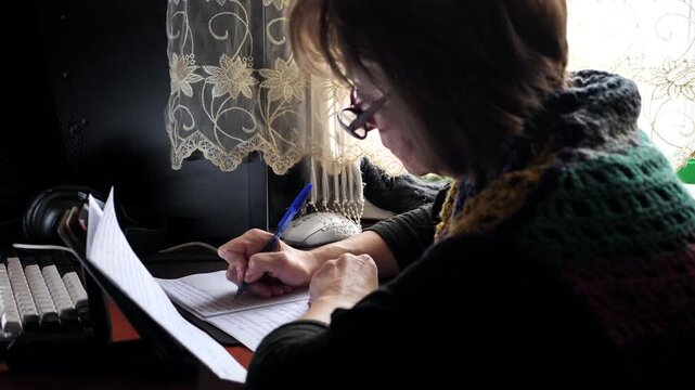 A woman writes with a pen in a notebook while sitting at a table.