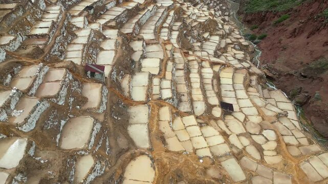 Aerial drone view of the Maras salt mines near Cusco, Peru, featuring hundreds of cascading salt terraces spread across the mountainside
