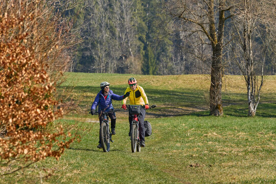 Happy senior couple enjoying an active lifestyle, riding electric bikes on a forest trail in spring. Outdoor recreation, healthy aging, and leisure time in nature on a sunny day.