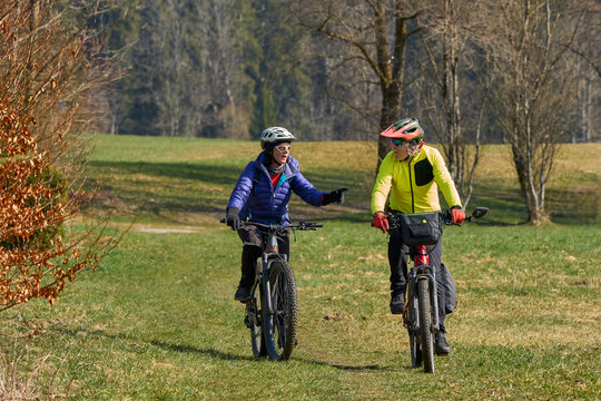 Happy senior couple enjoying an active lifestyle, riding electric bikes on a forest trail in spring. Outdoor recreation, healthy aging, and leisure time in nature on a sunny day.