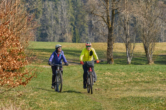 Happy senior couple enjoying an active lifestyle, riding electric bikes on a forest trail in spring. Outdoor recreation, healthy aging, and leisure time in nature on a sunny day.