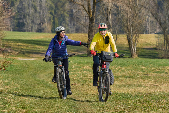Happy senior couple enjoying an active lifestyle, riding electric bikes on a forest trail in spring. Outdoor recreation, healthy aging, and leisure time in nature on a sunny day.