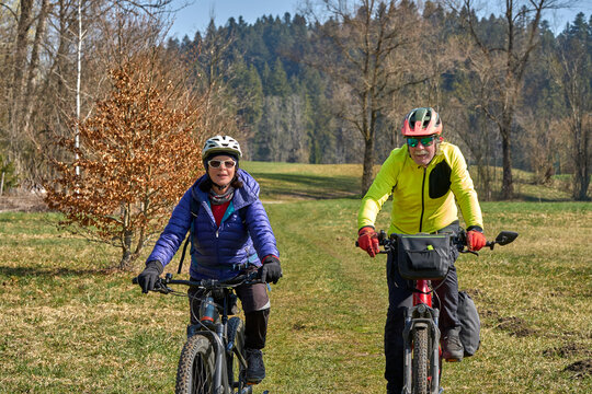 Happy senior couple enjoying an active lifestyle, riding electric bikes on a forest trail in spring. Outdoor recreation, healthy aging, and leisure time in nature on a sunny day.