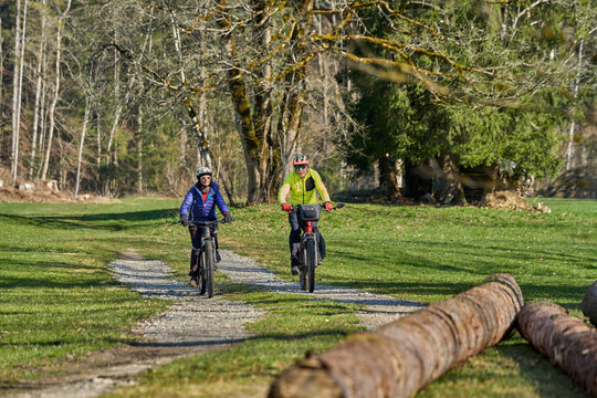 Happy senior couple enjoying an active lifestyle, riding electric bikes on a forest trail in spring. Outdoor recreation, healthy aging, and leisure time in nature on a sunny day.
