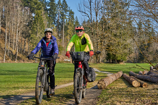 Happy senior couple enjoying an active lifestyle, riding electric bikes on a forest trail in spring. Outdoor recreation, healthy aging, and leisure time in nature on a sunny day.