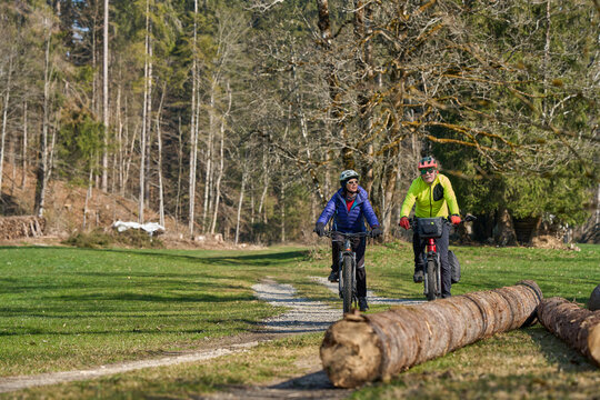 Happy senior couple enjoying an active lifestyle, riding electric bikes on a forest trail in spring. Outdoor recreation, healthy aging, and leisure time in nature on a sunny day.